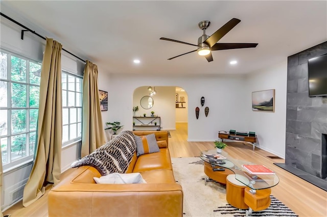 living room featuring a tiled fireplace, ceiling fan, and light hardwood / wood-style flooring