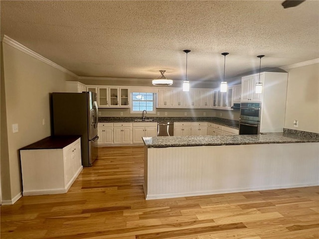 kitchen with kitchen peninsula, appliances with stainless steel finishes, pendant lighting, white cabinets, and sink