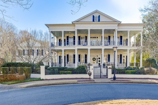 greek revival inspired property featuring a balcony, a fenced front yard, a gate, and a porch