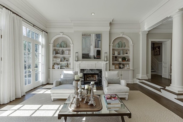 living area with decorative columns, built in features, a premium fireplace, wood finished floors, and crown molding