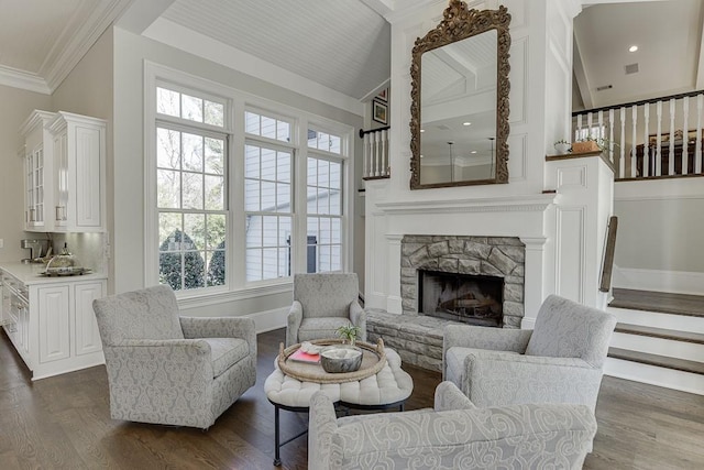 living area with dark wood-style flooring, lofted ceiling, ornamental molding, a stone fireplace, and stairs