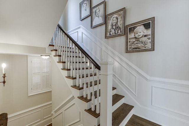 stairway with a wainscoted wall, a decorative wall, and wood finished floors