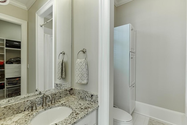 bathroom featuring baseboards, toilet, crown molding, vanity, and a closet