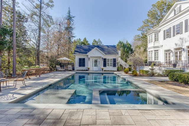 view of swimming pool featuring an outbuilding, a pool with connected hot tub, an exterior structure, and a patio