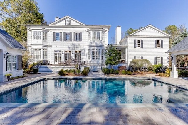 back of property with a chimney and an outdoor pool