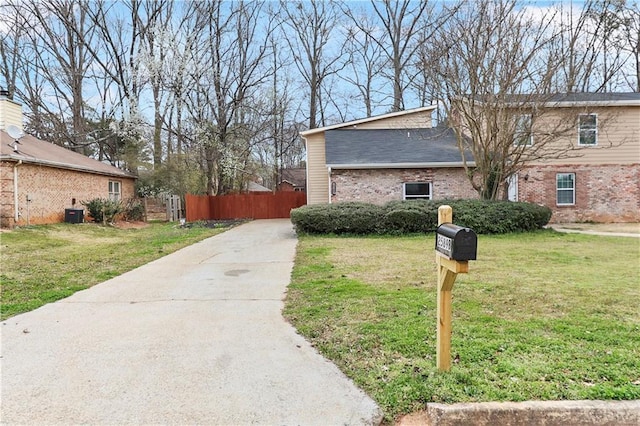 view of side of property featuring brick siding, a yard, driveway, and fence