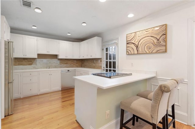 kitchen with white cabinetry, kitchen peninsula, white dishwasher, a breakfast bar, and light wood-type flooring