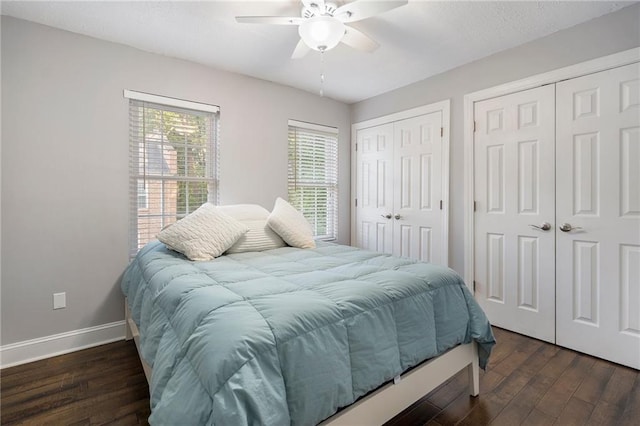 bedroom with dark hardwood / wood-style flooring, two closets, and ceiling fan