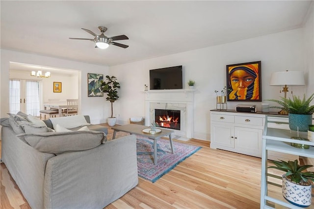 living room with french doors, a high end fireplace, light hardwood / wood-style floors, and ceiling fan with notable chandelier