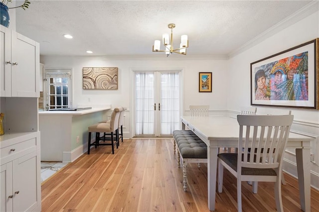 dining space with french doors, a notable chandelier, light wood-type flooring, a textured ceiling, and ornamental molding