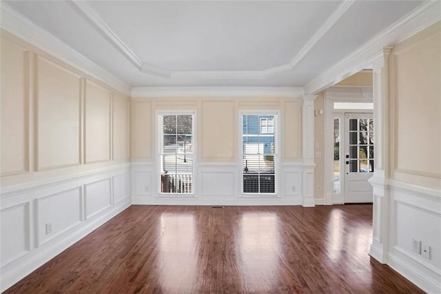 interior space with a raised ceiling, ornamental molding, dark wood-type flooring, and decorative columns