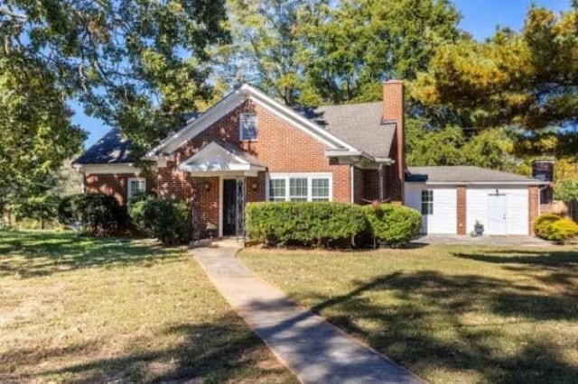 bungalow-style house featuring brick siding, a front yard, and a chimney