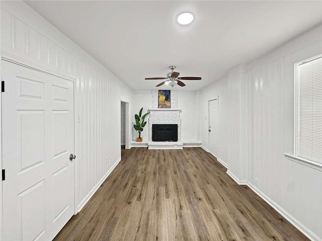 unfurnished living room with wood finished floors, a ceiling fan, a fireplace, a decorative wall, and baseboards
