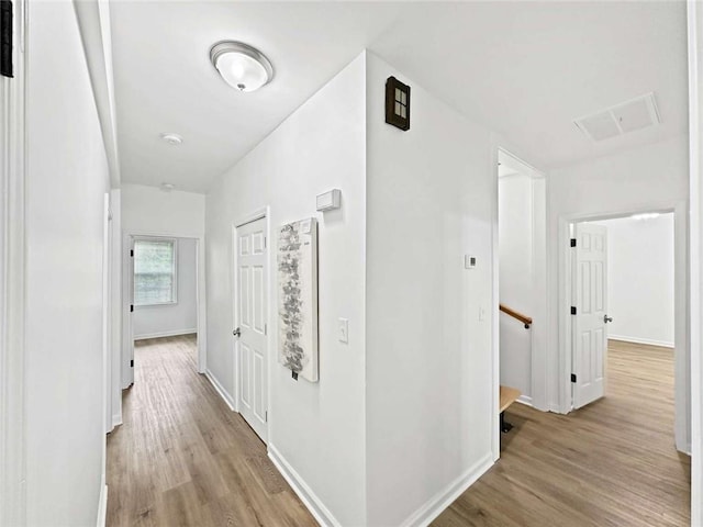 hallway featuring baseboards, light wood-type flooring, an upstairs landing, and visible vents