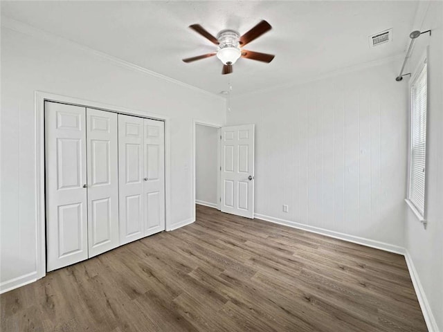 unfurnished bedroom featuring wood finished floors, a closet, crown molding, visible vents, and baseboards