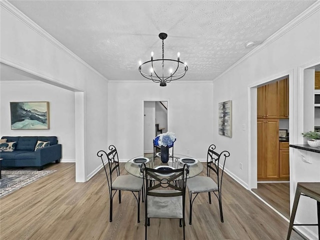 dining space featuring a chandelier, a textured ceiling, crown molding, and wood finished floors
