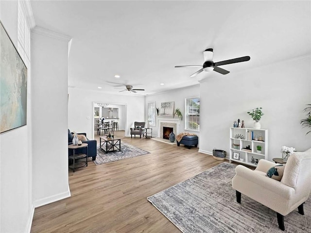 living area featuring wood finished floors, crown molding, baseboards, ceiling fan, and recessed lighting