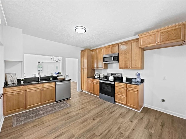 kitchen with a sink, dark countertops, light wood-style floors, appliances with stainless steel finishes, and a chandelier