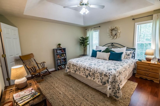 bedroom featuring dark wood finished floors, a raised ceiling, and ceiling fan