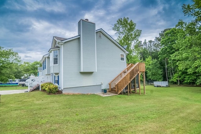 view of side of property featuring stairs, a chimney, a lawn, a deck, and view of scattered trees