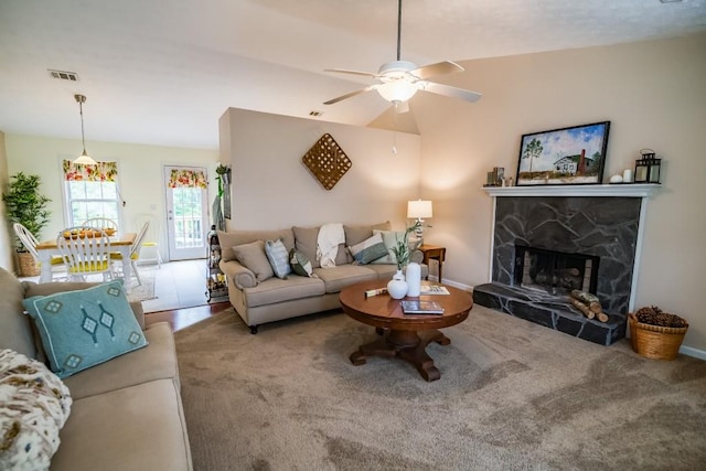 living area with a ceiling fan, carpet floors, a stone fireplace, and baseboards