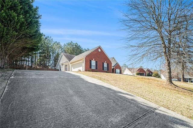 view of front of property featuring brick siding, a front lawn, fence, driveway, and an attached garage