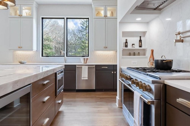 kitchen featuring stainless steel appliances, wine cooler, white cabinets, and wall chimney range hood