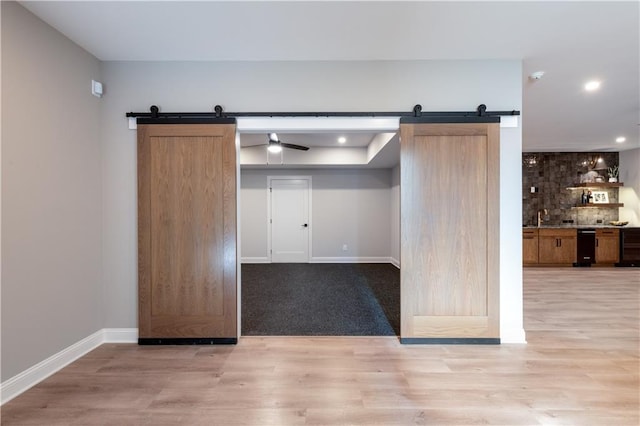 interior space with a barn door, light wood-type flooring, decorative backsplash, and baseboards