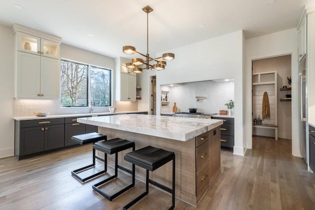 kitchen with light wood-style flooring, a kitchen island, tasteful backsplash, a kitchen bar, and glass insert cabinets