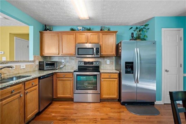 kitchen featuring stainless steel appliances, light stone countertops, a textured ceiling, sink, and tasteful backsplash