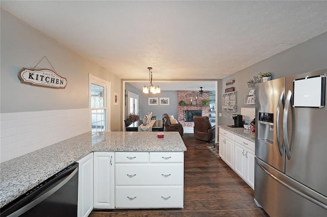 kitchen with dark wood finished floors, stainless steel fridge, white cabinets, a brick fireplace, and dishwasher