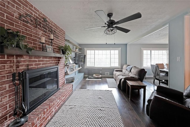 living room featuring a textured ceiling, wood finished floors, a fireplace, baseboards, and ceiling fan