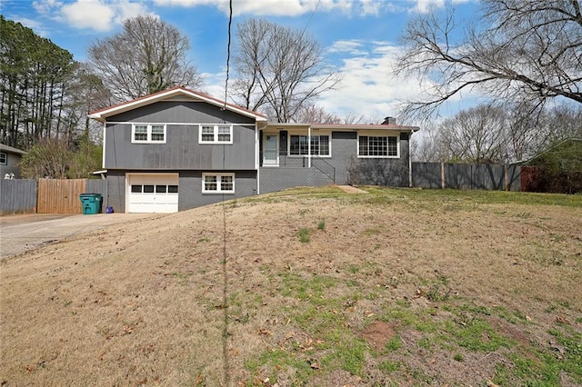 split level home with fence, concrete driveway, a garage, brick siding, and a chimney