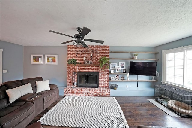 living area with a ceiling fan, a brick fireplace, wood finished floors, and a textured ceiling