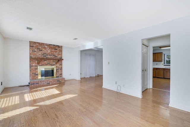 unfurnished living room featuring light hardwood / wood-style floors, a brick fireplace, and a textured ceiling