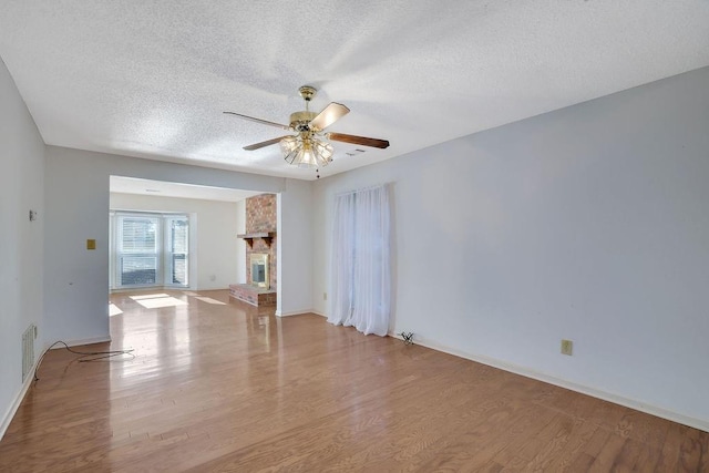 unfurnished living room with ceiling fan, a fireplace, light hardwood / wood-style floors, and a textured ceiling