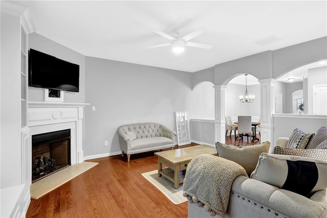 living area with decorative columns, ceiling fan, arched walkways, a fireplace with raised hearth, and wood finished floors