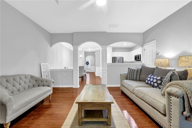 living room featuring arched walkways, ornate columns, a ceiling fan, and dark wood finished floors