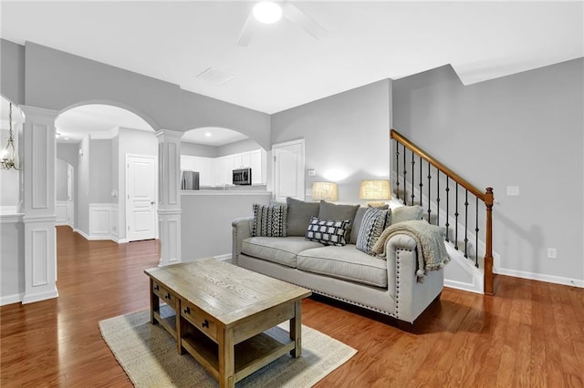 living area with arched walkways, ornate columns, a ceiling fan, stairway, and wood finished floors