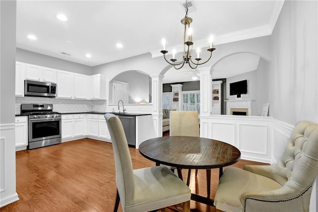 dining space featuring arched walkways, decorative columns, a fireplace, recessed lighting, and wood finished floors