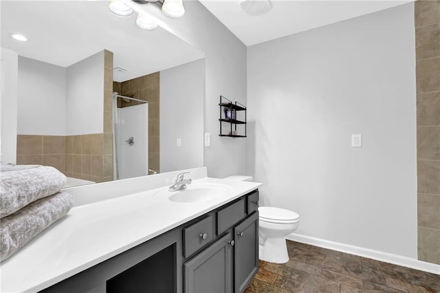 full bathroom with baseboards, toilet, stone finish floor, vanity, and tiled shower