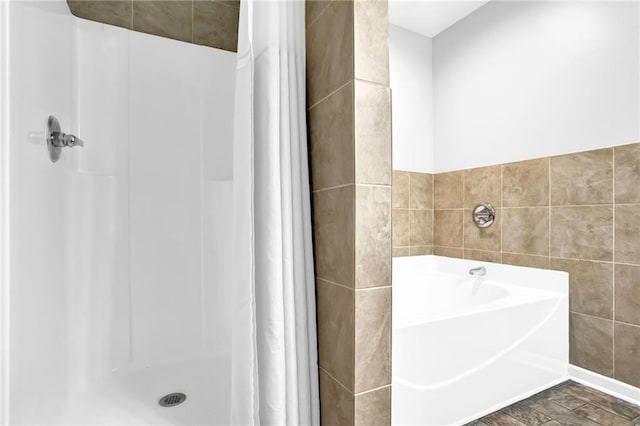 bathroom with tile walls, a stall shower, and a garden tub