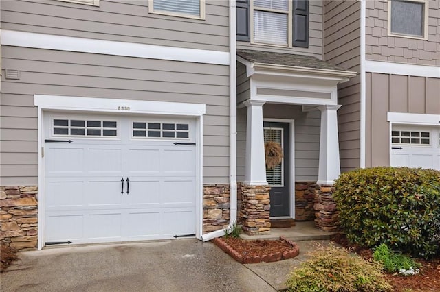property entrance with an attached garage, board and batten siding, driveway, and stone siding