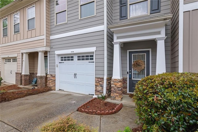 entrance to property featuring board and batten siding, an attached garage, stone siding, and driveway