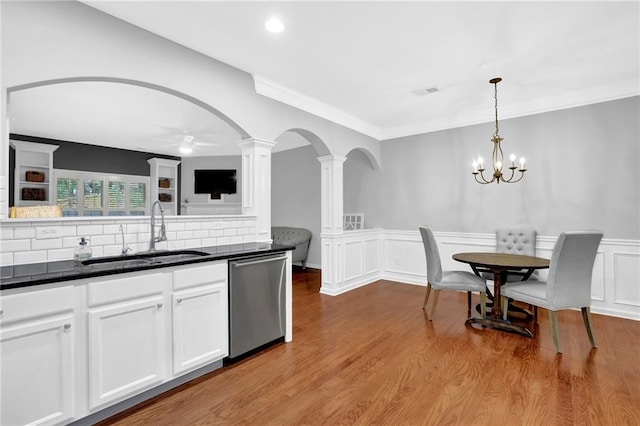 kitchen featuring dark countertops, ornate columns, stainless steel dishwasher, arched walkways, and a sink