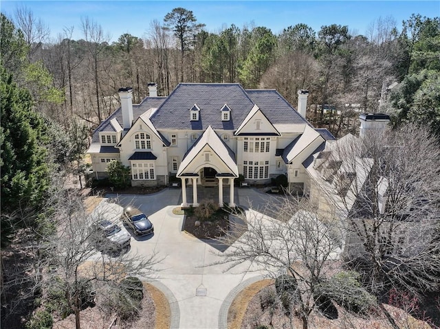 french country inspired facade with driveway, a chimney, and a forest view