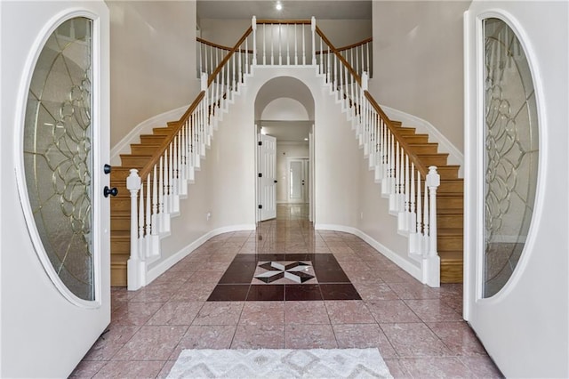 tiled foyer featuring stairs, arched walkways, baseboards, and a towering ceiling