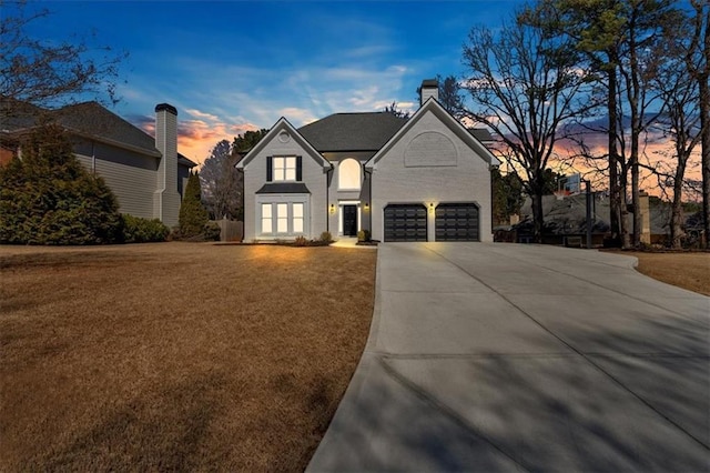 french country inspired facade featuring concrete driveway, a chimney, an attached garage, and a front yard