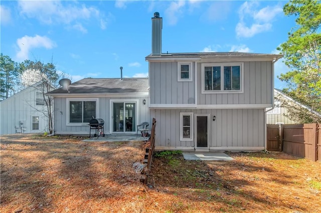 back of house featuring board and batten siding, a chimney, a patio, and fence