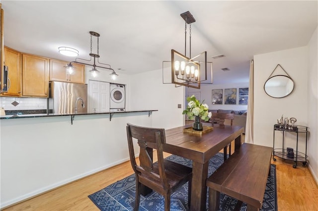 dining space featuring stacked washer and dryer, light wood finished floors, visible vents, and baseboards